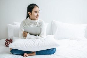 en ung kvinna som sitter på sin säng som rymmer en bärbar dator foto