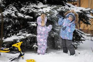 barn spela utomhus i snö. två liten systrar nära jul träd i vinter. foto