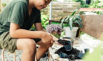 pojke händer skotta jord in i kastruller till förbereda växter för plantering fritid aktiviteter begrepp foto
