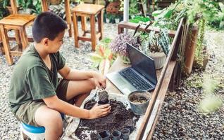 pojke lär till växa blommor i kastruller genom uppkopplad undervisning. skotta jord in i kastruller till förbereda växter för plantering fritid aktiviteter begrepp foto