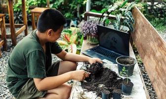 pojke lär till växa blommor i kastruller genom uppkopplad undervisning. skotta jord in i kastruller till förbereda växter för plantering fritid aktiviteter begrepp foto