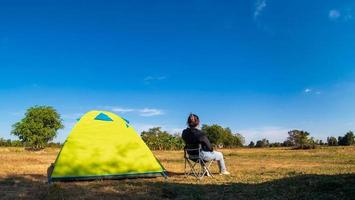 asiatiska kvinnliga turister sitter glada fria med grönt tält för resenären sitter på brett fält, med utsikt över kvällen i privat område thailand för camping tillflyktsort under lång semester för resor. foto