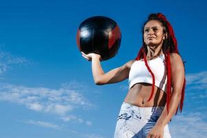 bakgrund himmel. atletisk kvinna med Med boll. styrka och motivation.photo av sportig kvinna i modern sportkläder foto