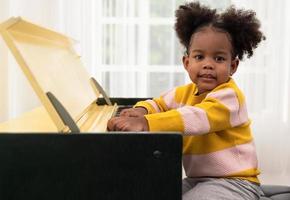 Lycklig liten lockigt svart flicka spelar piano på Hem foto