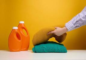 tvättades vikta kläder och plast orange stor flaskor med flytande rengöringsmedel stå på en vit tabell, gul bakgrund. rutin- läxa foto