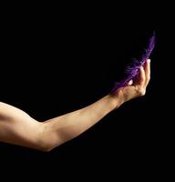kvinna hand är böjd på de armbåge, de muskler är spänd och håll en blå fjäder på en mörk bakgrund foto