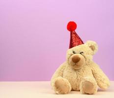 ledsen teddy beige Björn i en röd keps sitter på en lila bakgrund foto