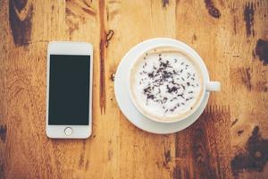 en kopp kaffe och smartphone på träbord i café
