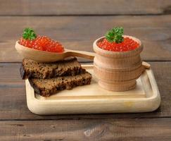röd lax kaviar lögner på en bit av råg bröd. brun trä- tabell foto