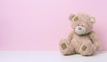 brun teddy Björn med plåster sitter på en vit tabell, rosa bakgrund foto