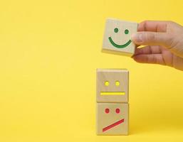 trä- block med annorlunda känslor från leende till sorg och en kvinnas hand. begrepp för bedöma de kvalitet av en produkt eller service foto