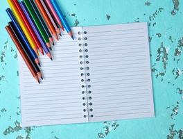 öppen anteckningsbok i en linje och flerfärgad trä- pennor foto