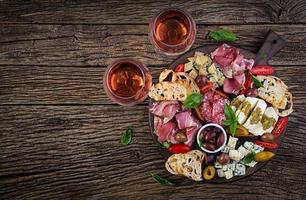 antipasto tallrik med skinka, skinka, salami, blå ost, mozzarella med pesto och oliver på en trä- bakgrund. topp se, över huvudet foto