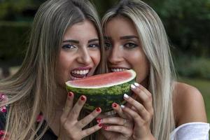 par av ung skön kvinnor äter en skiva av färsk vattenmelon foto