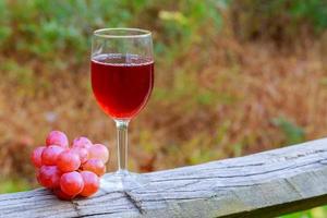 rött vin glas och klase av druvor på träbord foto