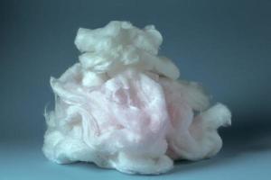 rosa bomull ull på en blå bakgrund. en mjuk lugg av fiber.stycke bomull ull isolerat på blå foto