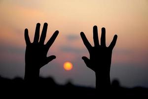 silhuett av mänsklig hand Uppfostrad till göra en önskar, solnedgång bakgrund foto