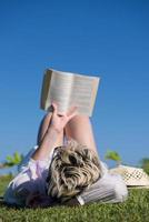 kvinna liggande och läsning henne favorit bok på en äng täckt med färsk grön gräs på en solig sommar eller vår dag. foto