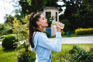 ung kvinna i en sportslig kostym drycker från en flaska efter en träna foto