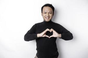 en Lycklig ung asiatisk man bär en svart skjorta känner romantisk former hjärta gest uttrycker anbud känslor foto