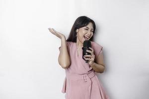 porträtt av sorglös asiatisk kvinna, har roligt karaoke, sång i mikrofon medan stående över vit bakgrund foto