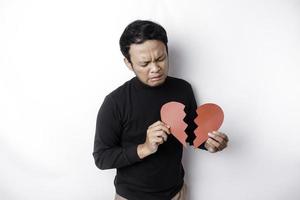 skön ung asiatisk man uttryckt hans sorg medan innehav bruten hjärta isolerat på vit bakgrund foto