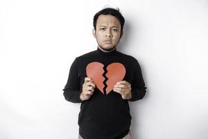 skön ung asiatisk man uttryckt hans sorg medan innehav bruten hjärta isolerat på vit bakgrund foto