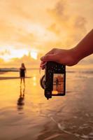 en kamera med händer fotografier en balinesisk kvinna håller på med en gymnastiska rörelse på en svart skjorta nära de strand foto