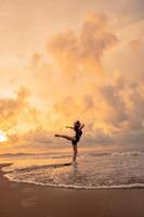 en ballerina i en svart klänning är praktiserande balett rör sig på de strand med mycket flexibel rörelser med en se av de moln Bakom foto