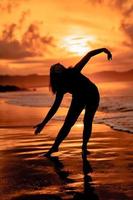de silhuett av ett indonesiska tonåring dans mycket flexibelt med de kraschar vågor på de strand foto