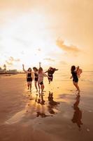 en grupp av asiatisk tonåringar löpning med Lycklig uttryck på semester med deras vänner full på de strand foto