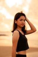 ett asiatisk tonåring med en söt ansikte i svart kläder ler medan njuter de skön landskap på de strand foto