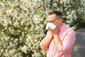 en man nyser in i en näsduk mot de bakgrund av blommande träd foto