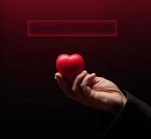 en mannens hand innehar en röd hjärta på en mörk bakgrund, en plats för ett inskrift foto