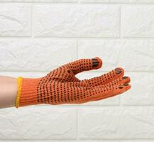 kvinna hand i ett orange arbete skyddande handske mot de bakgrund av en vit tegel vägg, de hand villkorligt innehar ett objekt foto