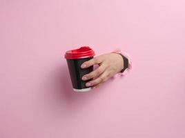 hand innehar papper kartong brun kopp för kaffe, rosa bakgrund foto