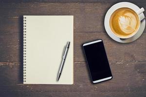 topp se anteckningsbok, penna, kaffe kopp, och telefon på trä tabell, årgång filtrera. foto
