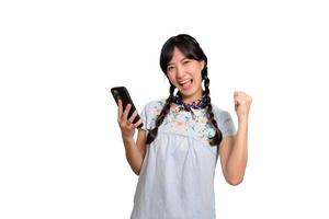 porträtt av Lycklig skön ung asiatisk kvinna i denim klänning använder sig av en smartphone på vit bakgrund. studio skott foto