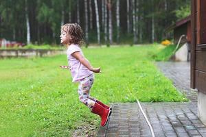 flicka spelar i regnig väder barn Hoppar i pöl och lera i de regn. foto