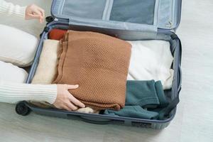 kvinna hand förpackning henne vinter- kläder i bagage. tid till resa, resa, koppla av, vår eller höst eller vinter- säsong och semester begrepp foto