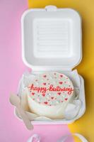 en små bento födelsedag kaka i en låda med en trä- sked. gul och rosa bakgrund foto