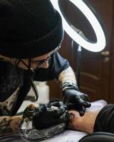 professionell tatuering konstnär saker en tatuering på de mannens hand. tatuering konstnär på arbete. tatuering skapande bearbeta. konst och kreativitet foto
