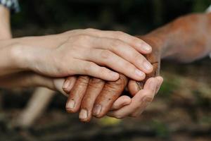 händer av de gammal man och en kvinna hand på de trä tabell i Sol ljus foto