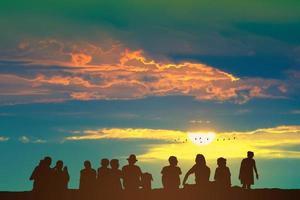 silhuett människor Sammanträde på de golv och soluppgång på de färgrik himmel orange moln och fåglar flygande foto