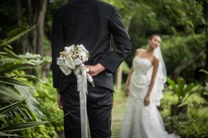 porträtt av en brudgum som gömmer en blommig bukett bakom ryggen för att överraska bruden foto