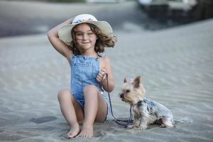 skön flicka Sammanträde på de strand sand innehav de koppel av henne sällskapsdjur yorkshire terrier. foto