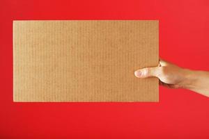 en tom ark av kartong i din händer på en röd bakgrund. foto
