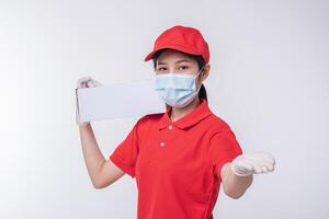 bild av en medveten ung leverans man i röd keps tom t-shirt enhetlig ansikte mask handskar stående med tömma vit kartong låda isolerat på ljus grå bakgrund studio foto