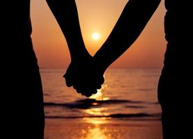 silhuett av ett par som håller händerna vid solnedgången foto