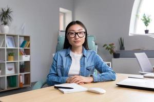 porträtt av ung företag kvinna i modern kontor, asiatisk ser på kamera leende foto